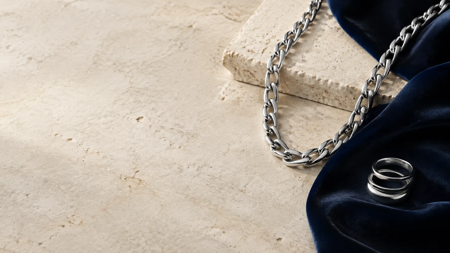 Silver-tone chain and rings styled on pale stone and navy fabric